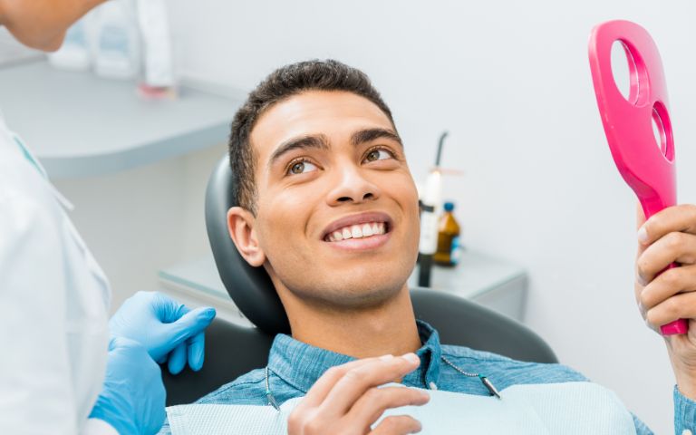 Smiling patient holding mirror after dental filling consultation at Cleopatra Dental