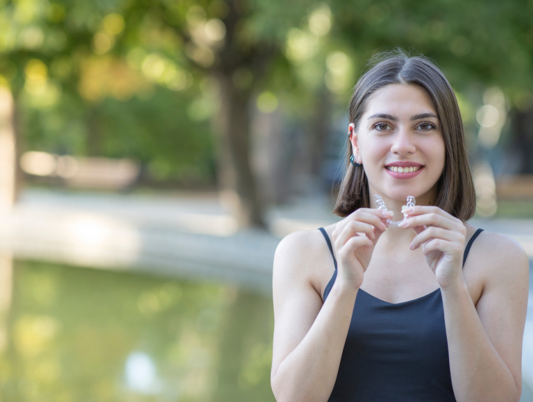 Woman patient holding clear aligners and smiling