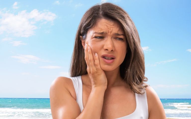 Woman holding her cheek in pain due to a dental emergency this summer