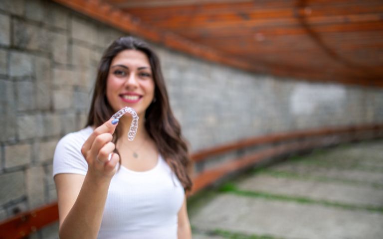 Woman smiling while holding clear aligners, ready for summer care tips.